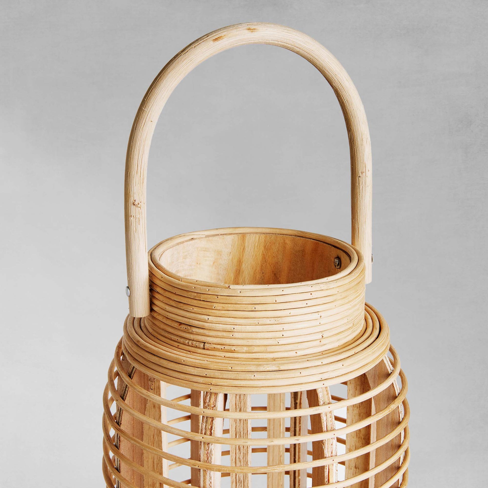 Rattan cylinder lantern, closeup view of handle,  with gray background.
