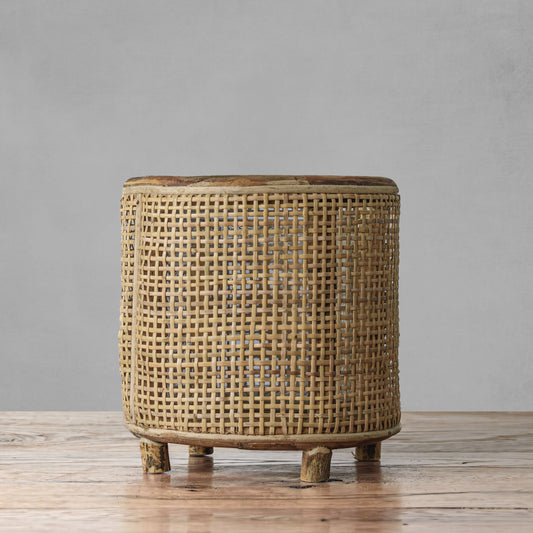Rattan round hurricane candle holder on wooden table with gray background.