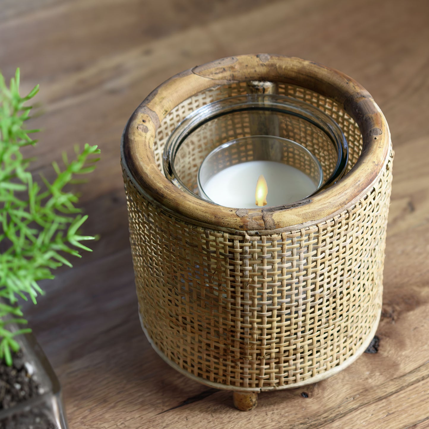 Rattan round hurricane candleholder on wooden table with rosemary.