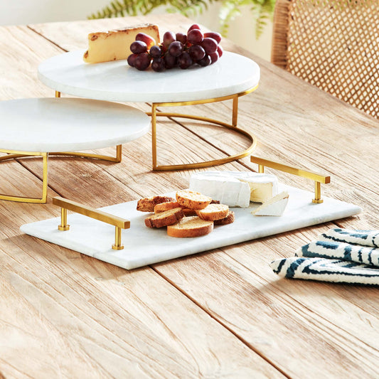 Rectangular marble serving tray with brass accents stylized with food on dining table.