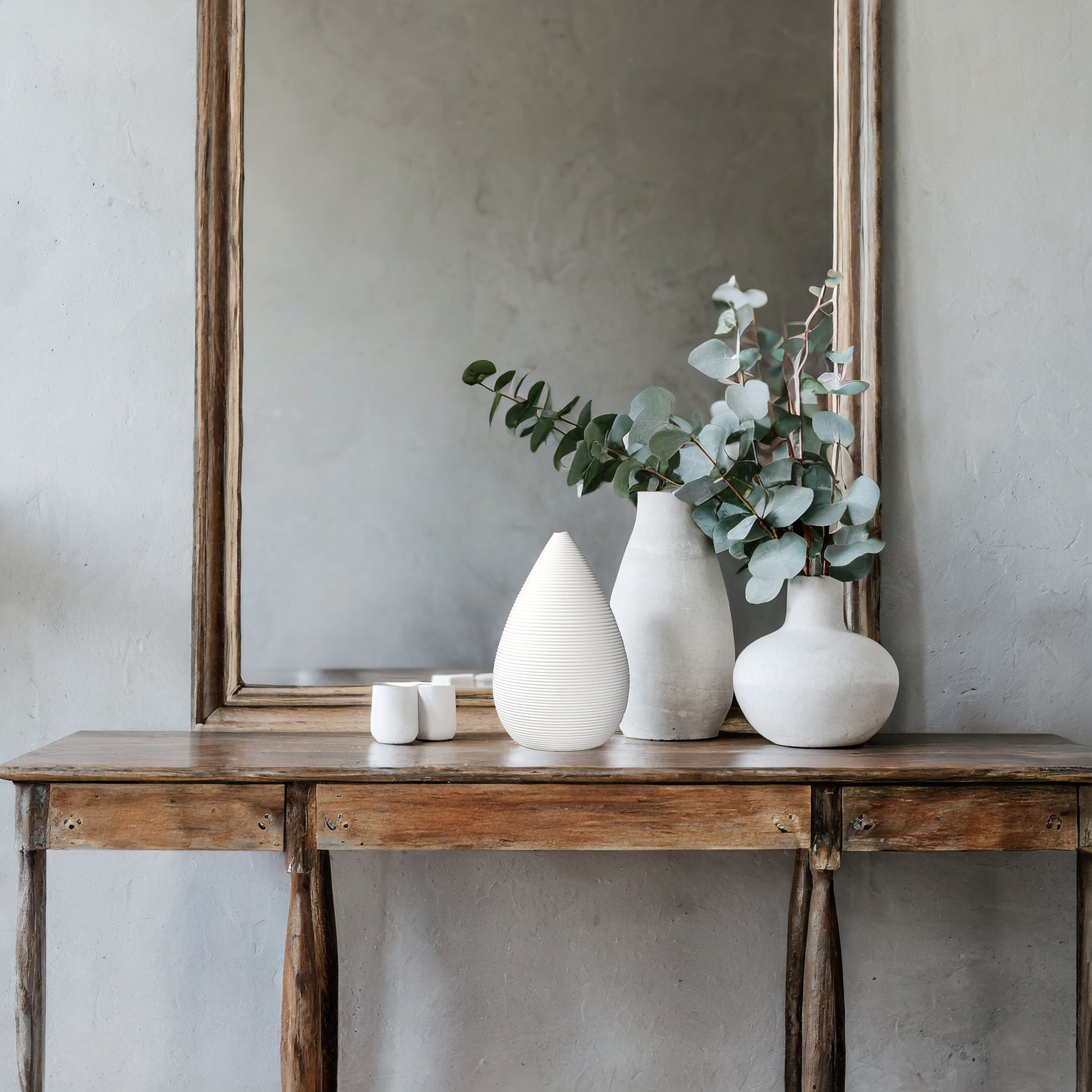 Tapered ribbed white ceramic vase on wood console table with white vases and mirror.