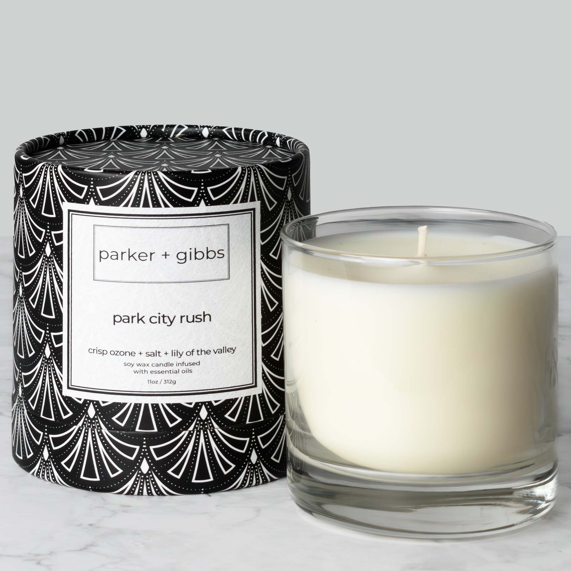 Luxury scented soy wax blend candle with ozone, salt, and lily of the valley essential oils on marble table with gray background.