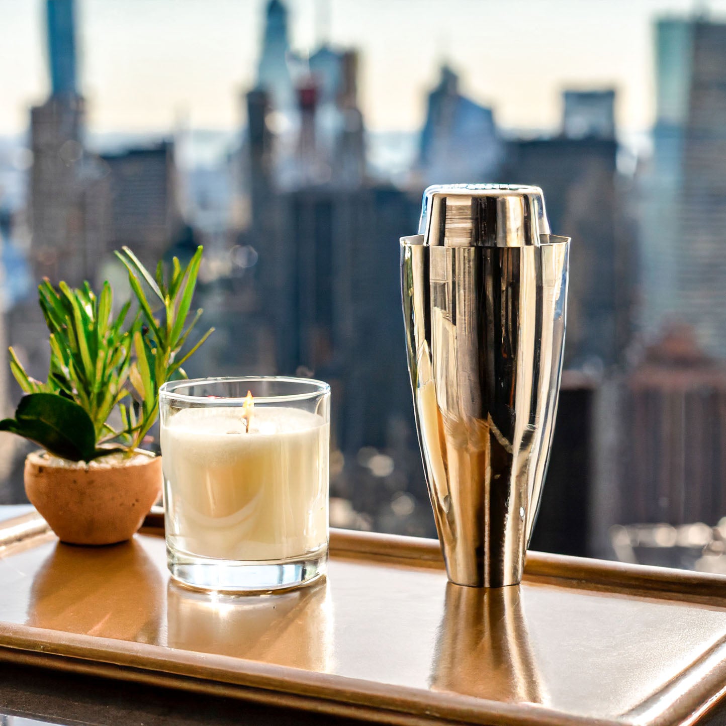 Scented soy wax blend candle on leather tray with martini shaker and Manhattan, New York City background.