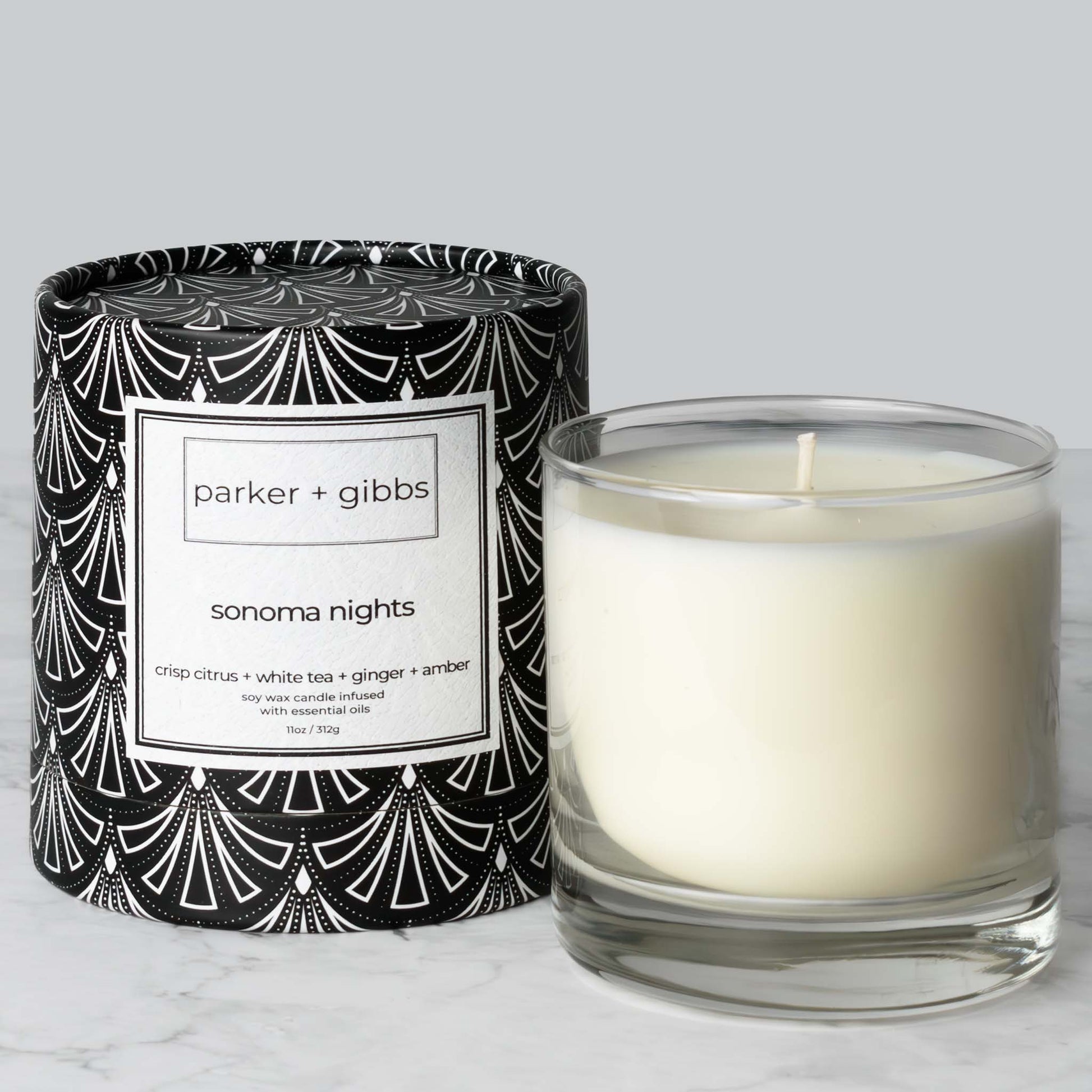 Luxury scented soy wax blend candle with citrus, white tea, ginger, and amber essential oils on marble table with gray background.