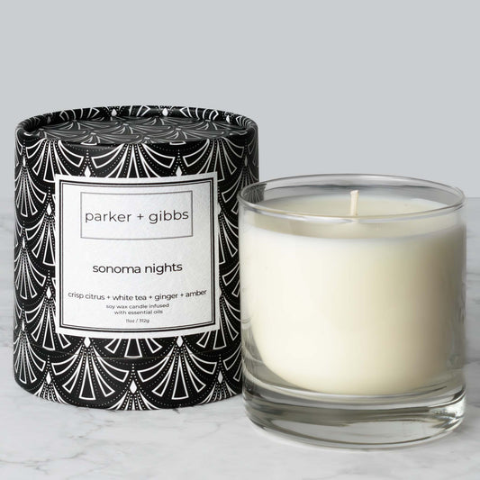 Luxury scented soy wax blend candle with citrus, white tea, ginger, and amber essential oils on marble table with gray background.