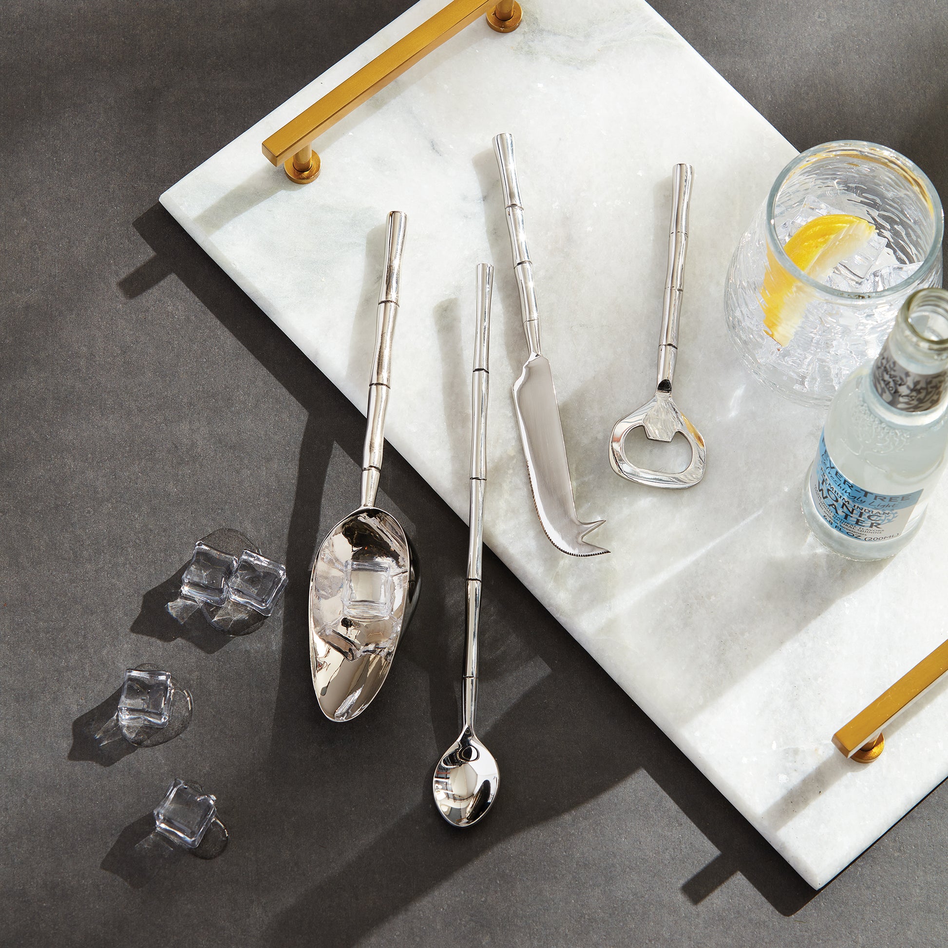 Stainless steel bamboo style barware tools set stylized with marble tray, ice, and glasses.