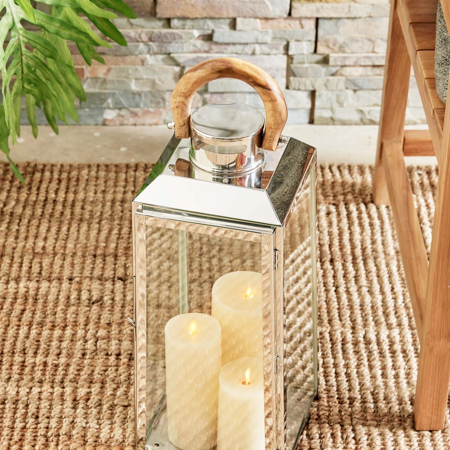 Large stainless steel outdoor lantern with teak wood handle and with flameless candles on sisal rug.