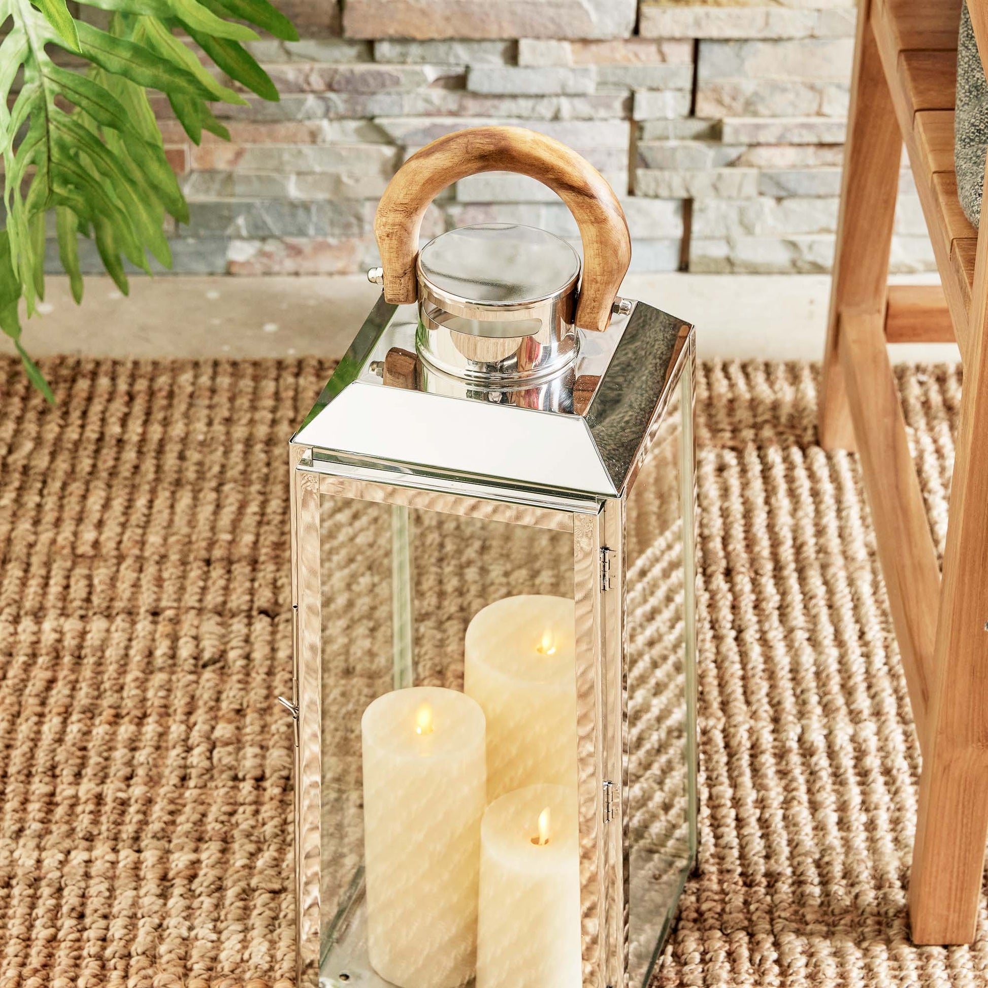Large stainless steel outdoor lantern with teak wood handle and with flameless candles on sisal rug.