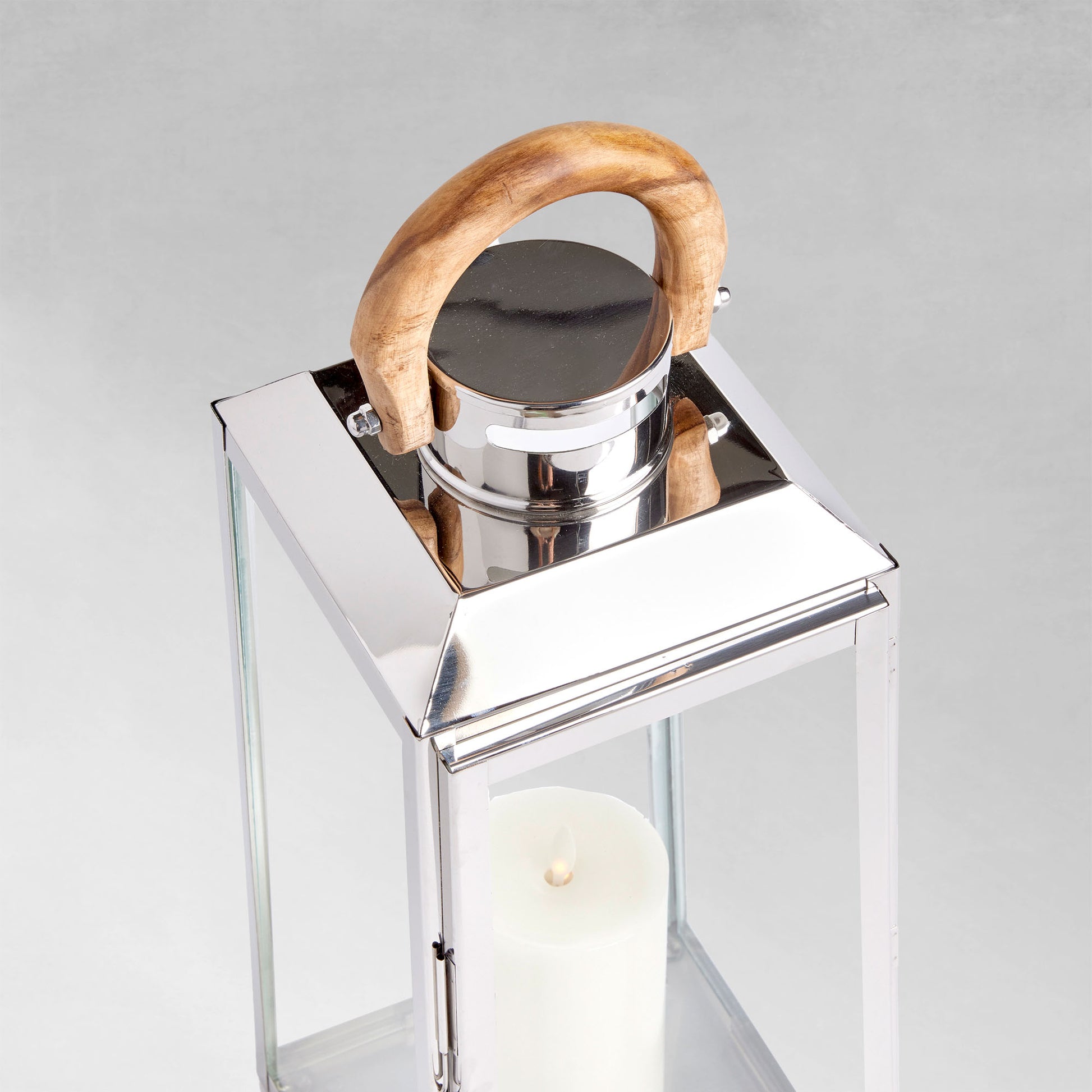 Large stainless steel outdoor lantern with teak wood handle, closeup view, on gray background.