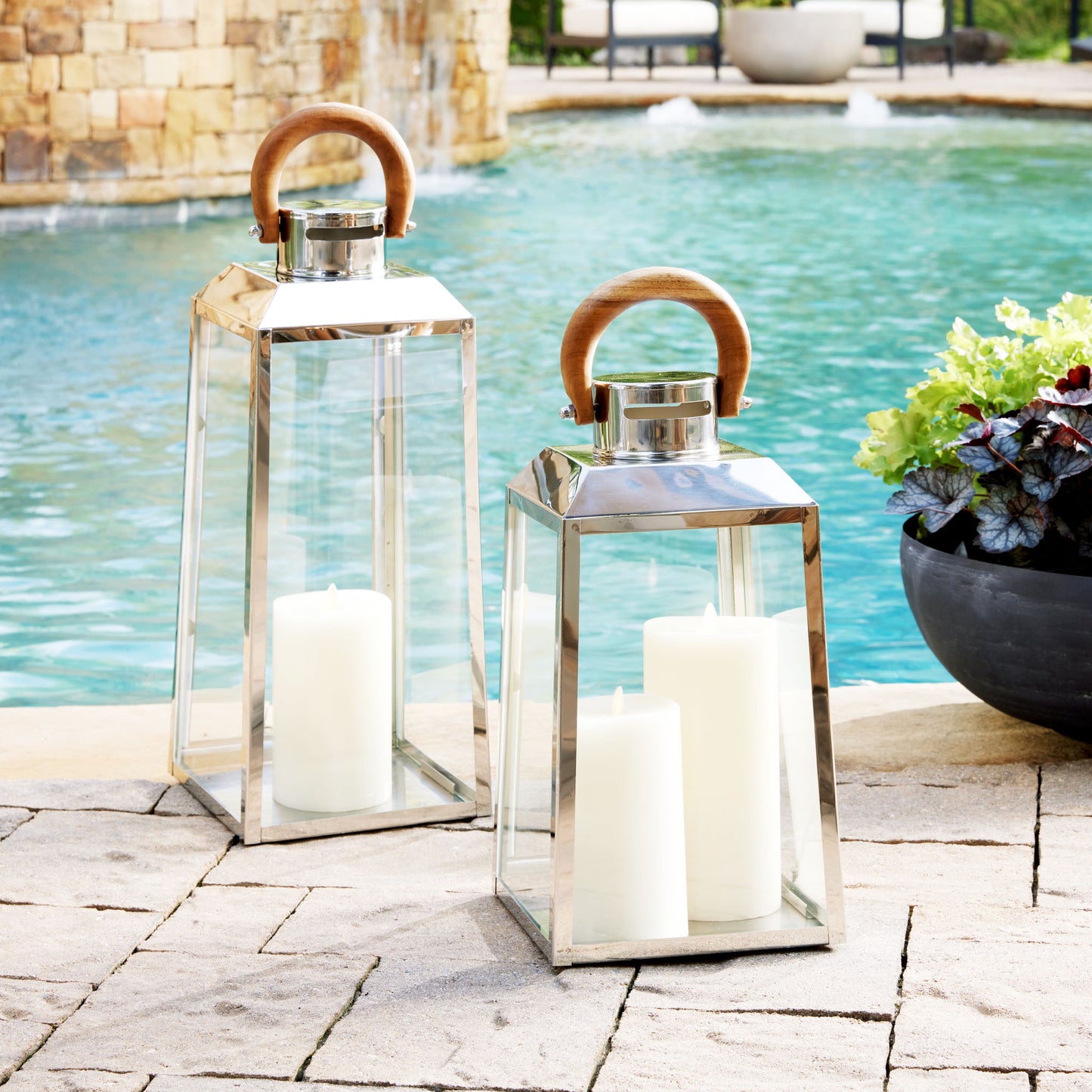 Small and large stainless steel lanterns with teak wood handle next to pool.