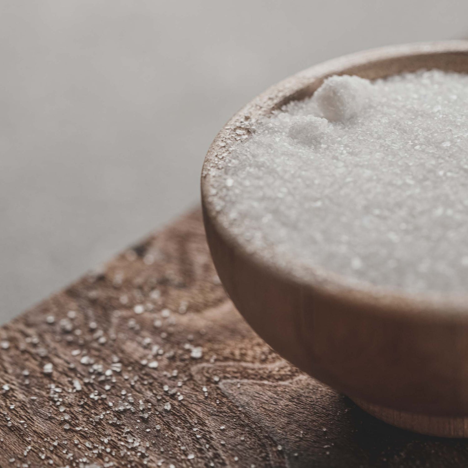 Sugar in wooden bowl on top of wooden table.