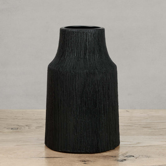 Textured ceramic small vase in matte black on wood table with gray background.