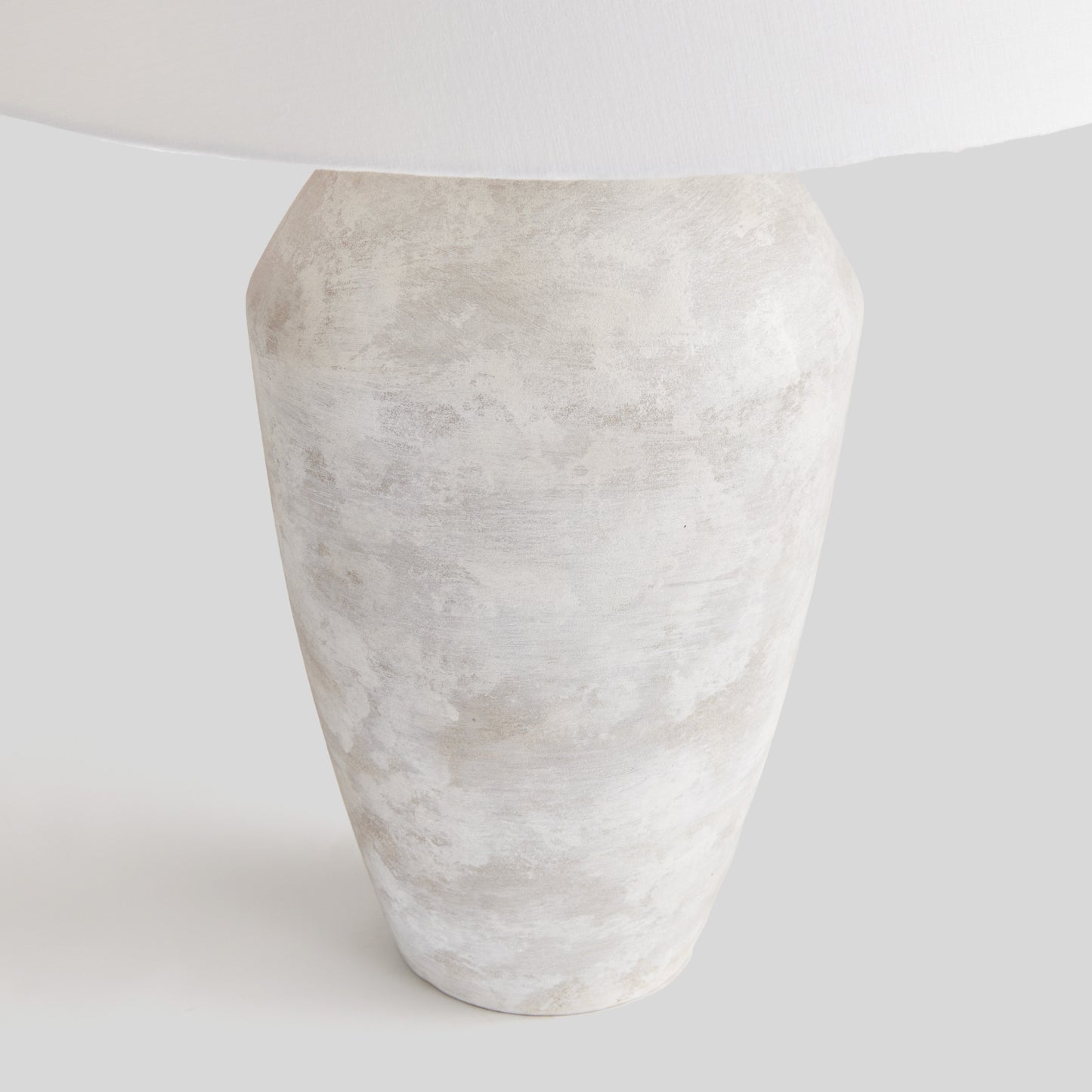 Closeup of lamp base for weathered gray ceramic table lamp with light gray background.