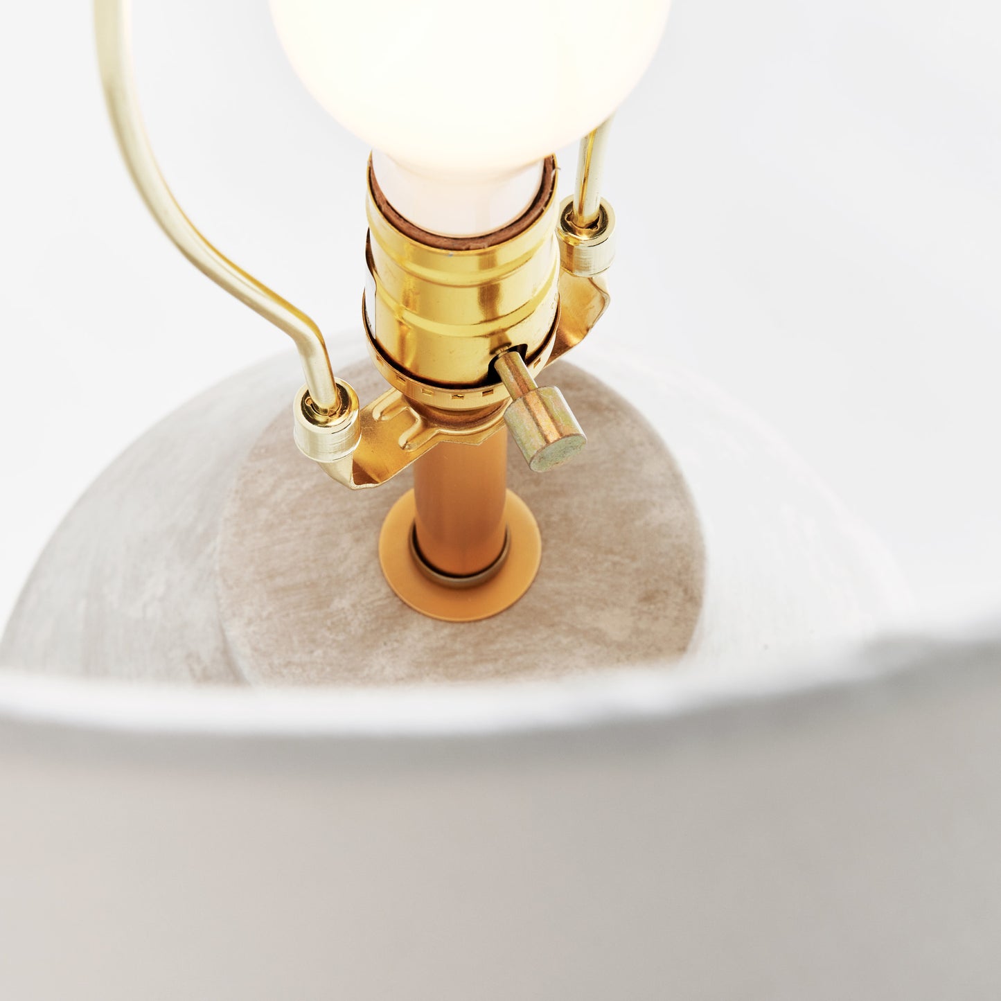 Weathered gray ceramic table lamp, closeup view of hardware, with light gray background.
