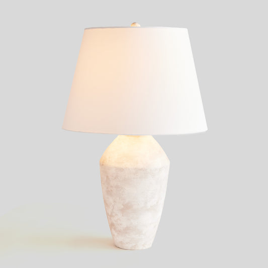 Illuminated weathered gray ceramic table lamp with light gray background.