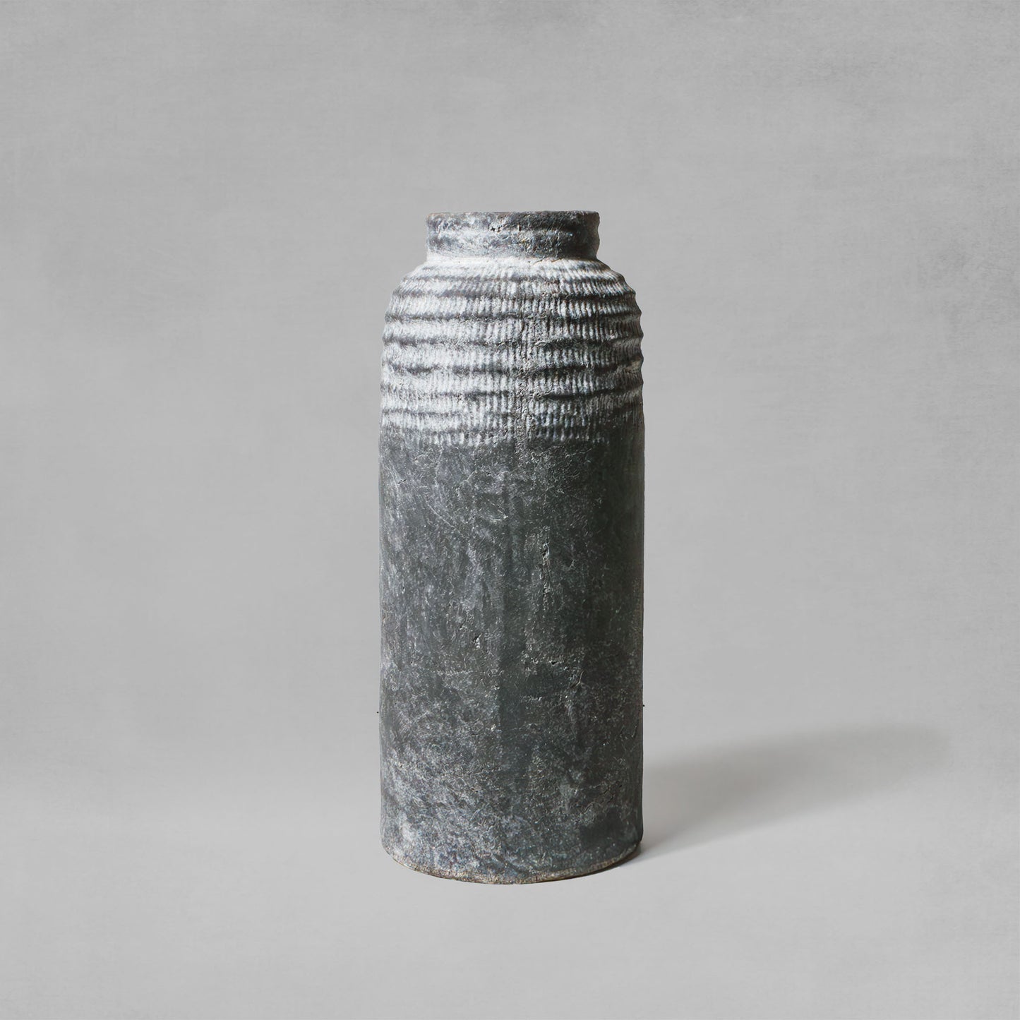 Large artisanal weathered gray earthenware vase with gray background.