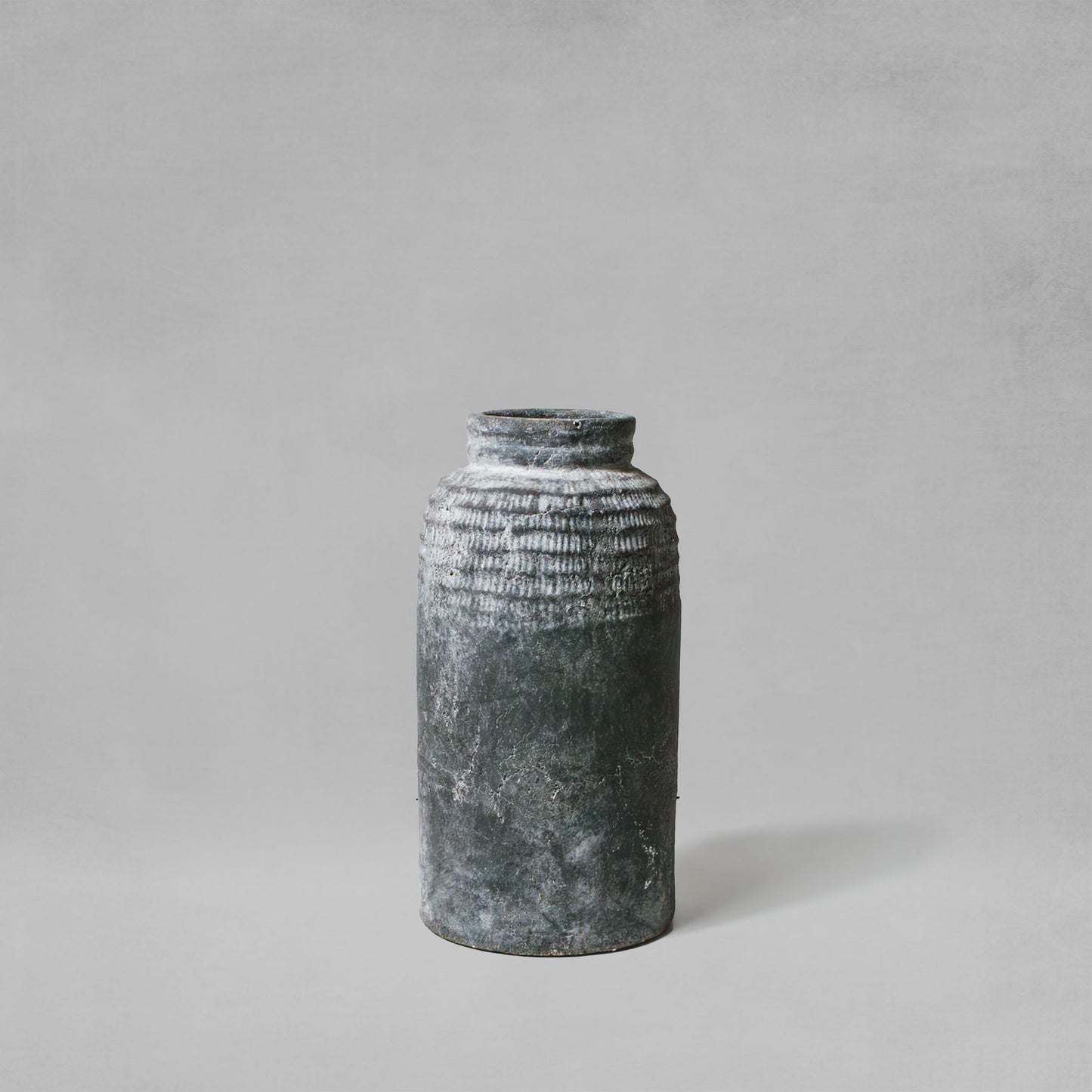 Medium artisanal weathered gray earthenware vase with gray background.