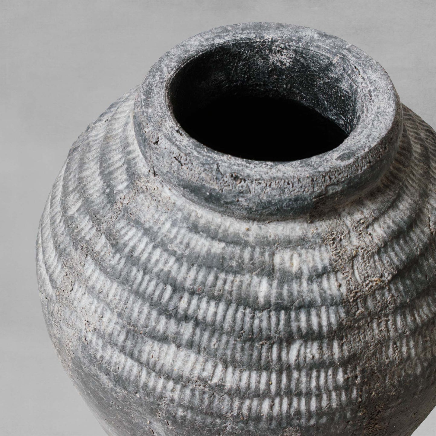 Closeup view of small artisanal weathered gray earthenware vase with gray background.