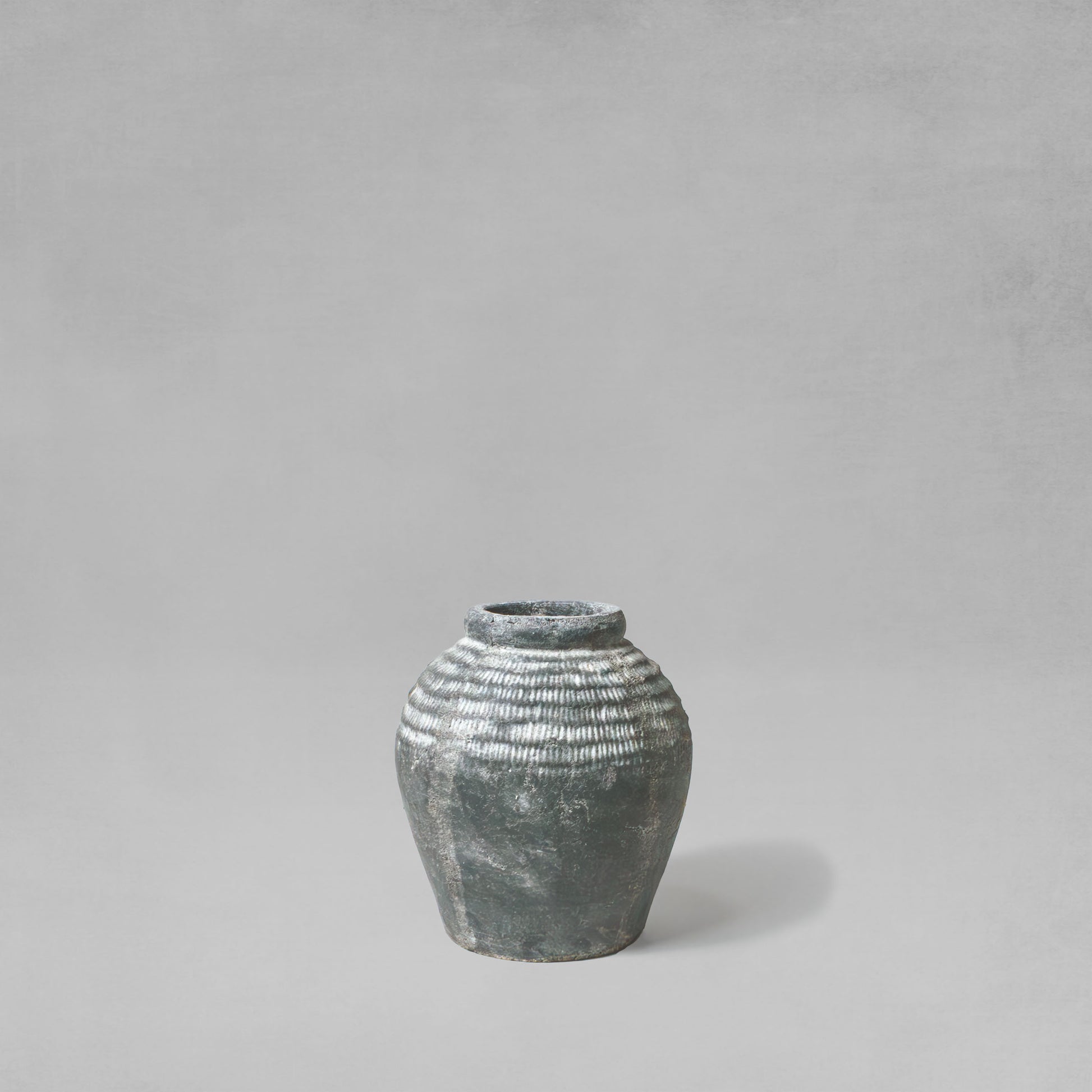 Small artisanal weathered gray earthenware vase with gray background.