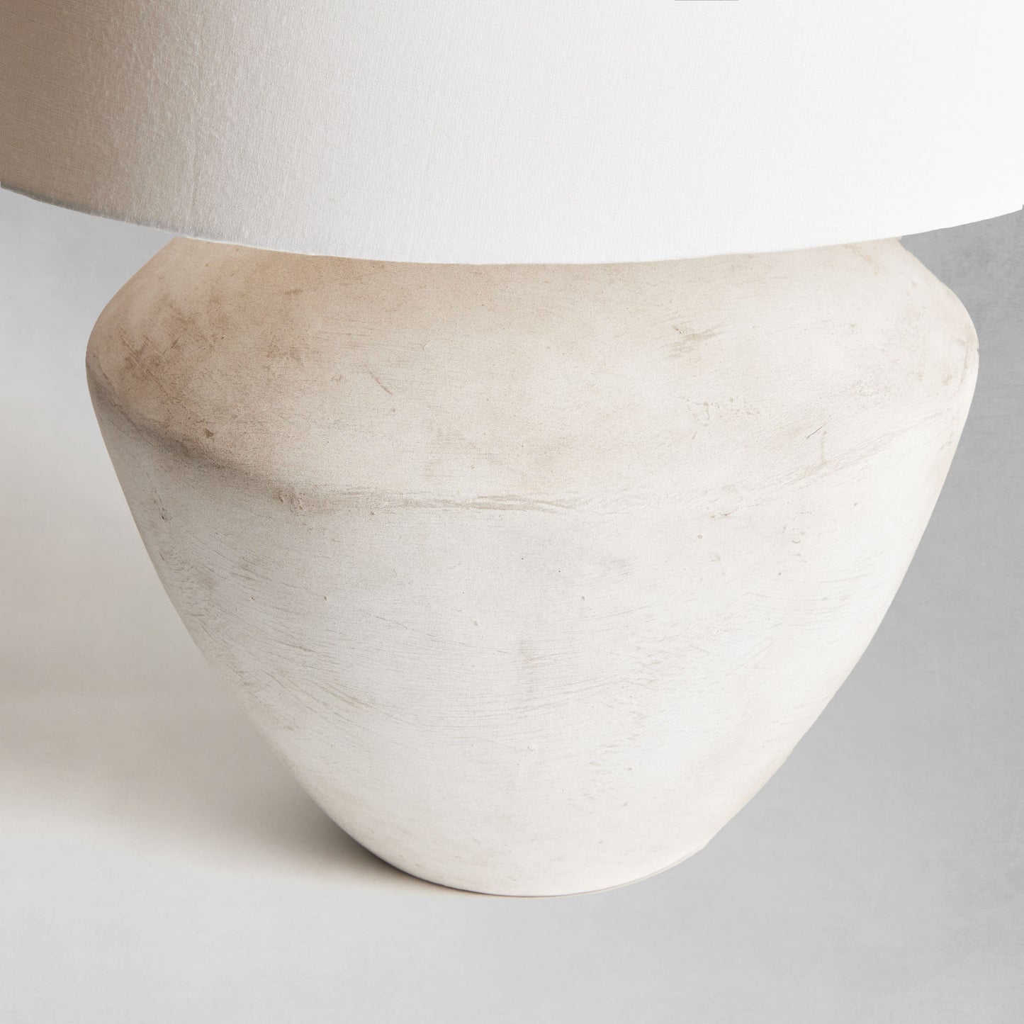 Weathered gray round ceramic table lamp, closeup view of lamp base, with gray background.