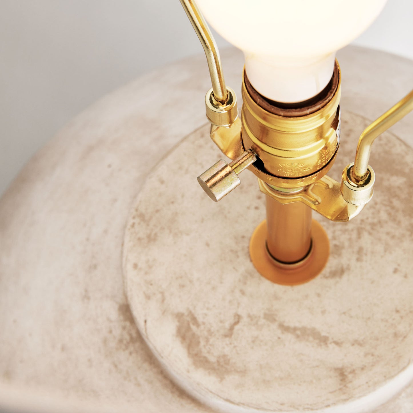 Weathered gray round ceramic table lamp, closeup view of hardware, with gray background.