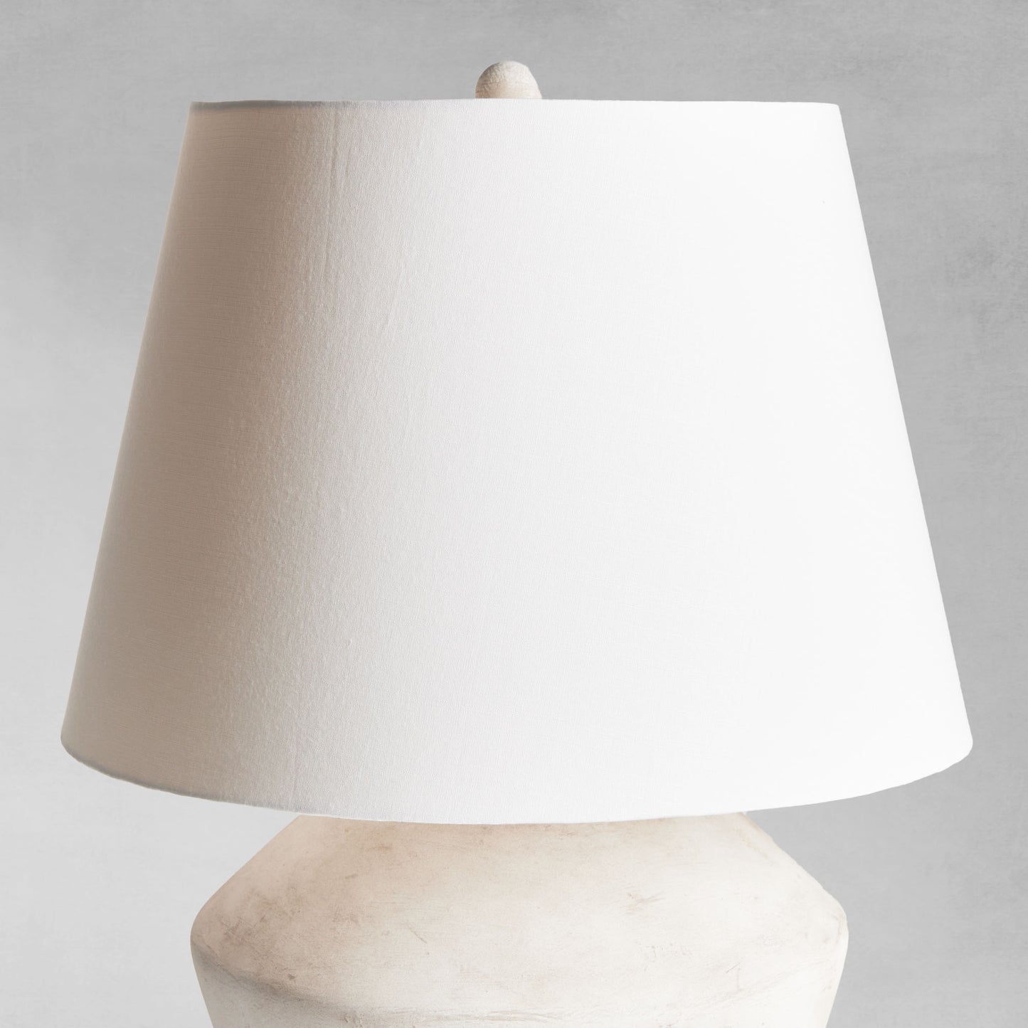 Weathered gray round ceramic table lamp, closeup view of shade, with gray background.