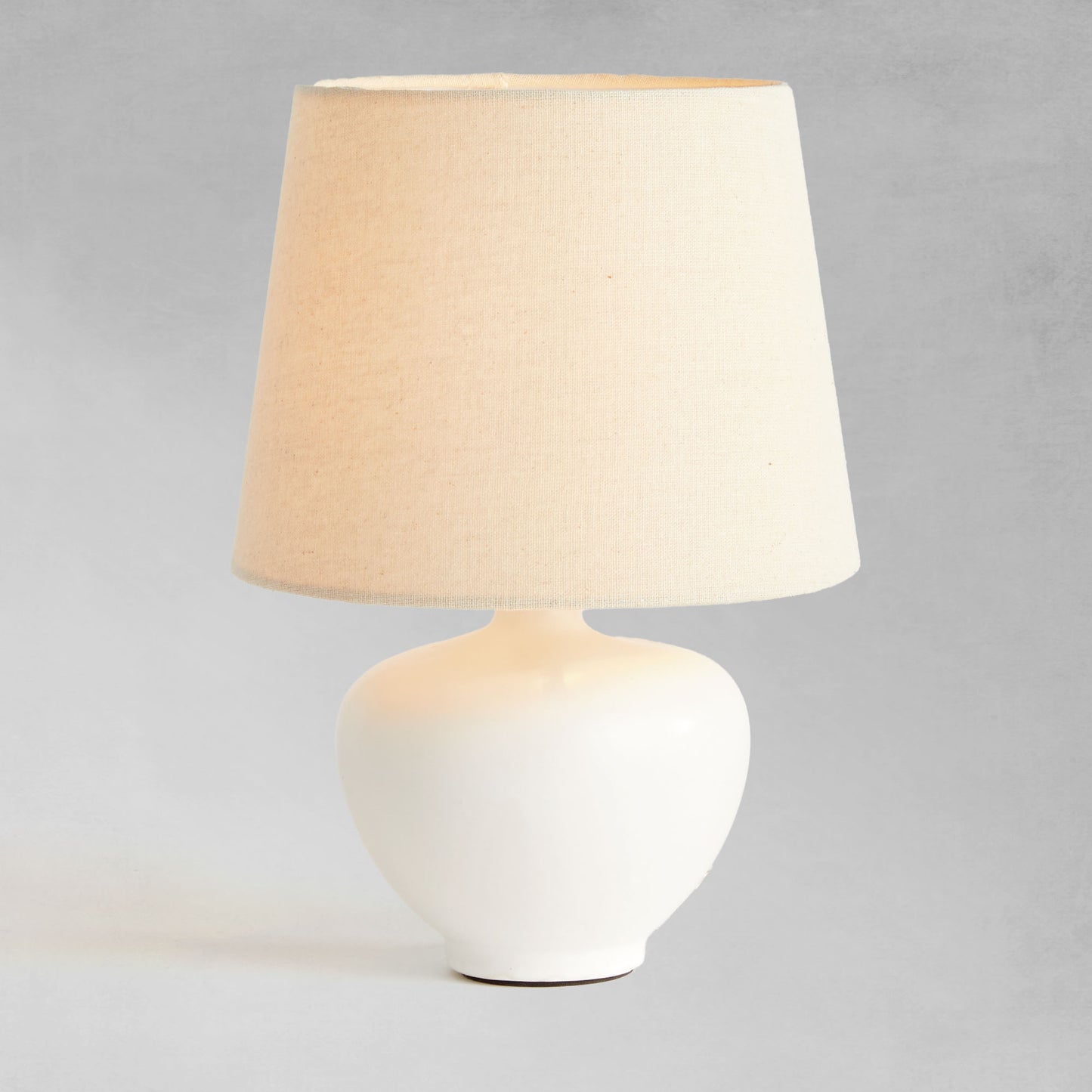 White ceramic mini lamp, illuminated, with gray background.