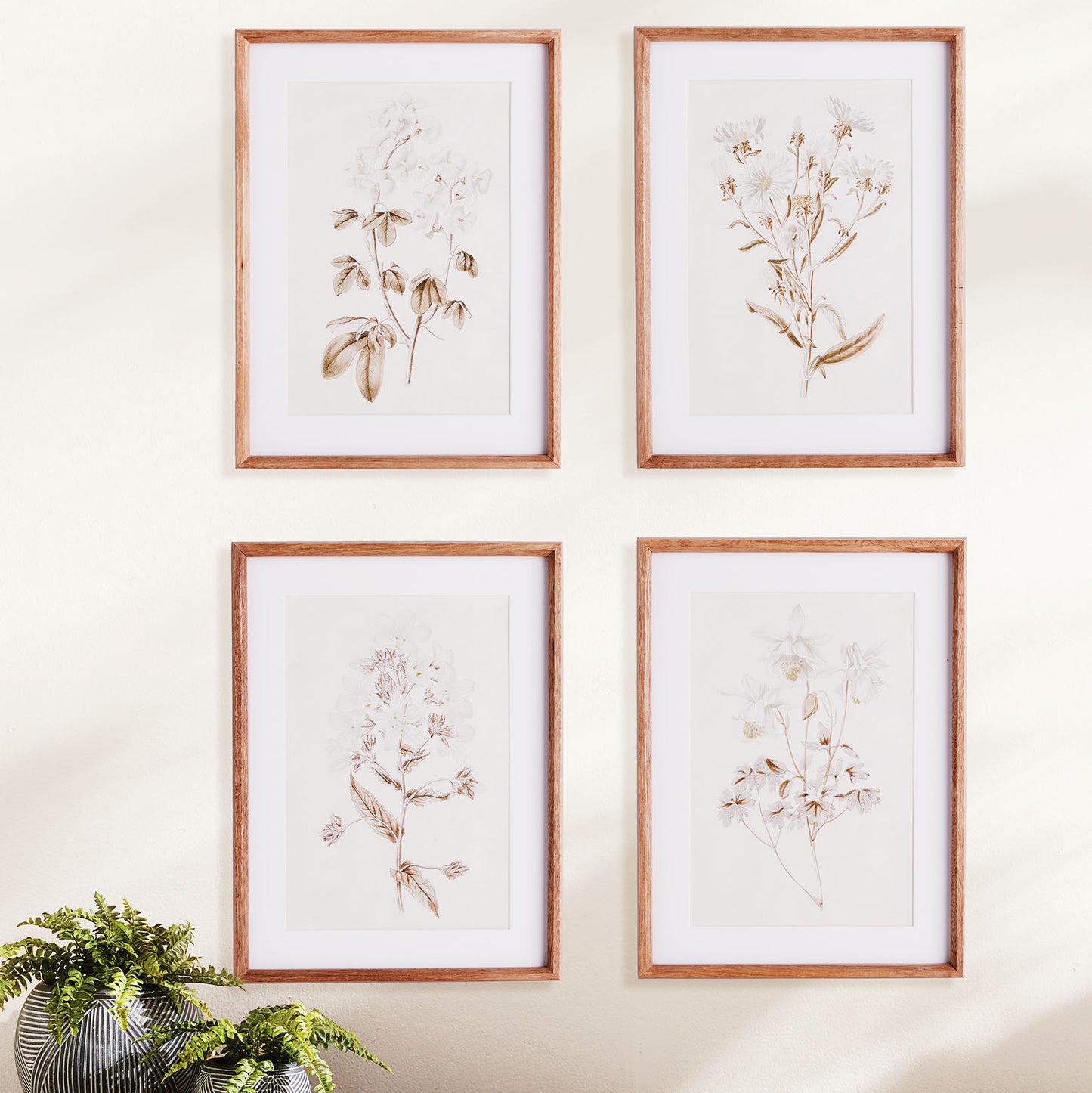White flowers gallery wall art set stylized above table with plants.