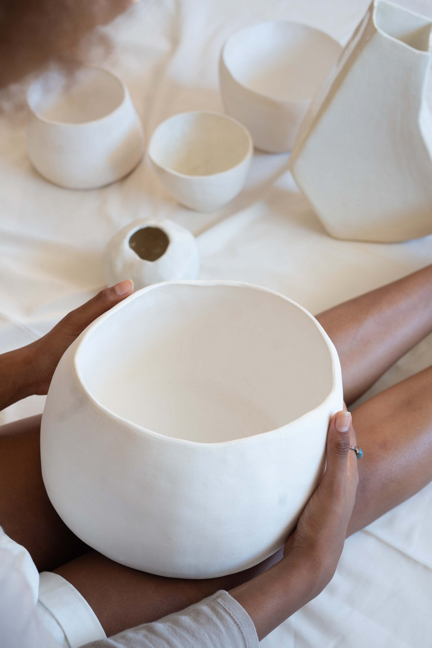 Woman holding white decorative ceramic bowl in her lap.