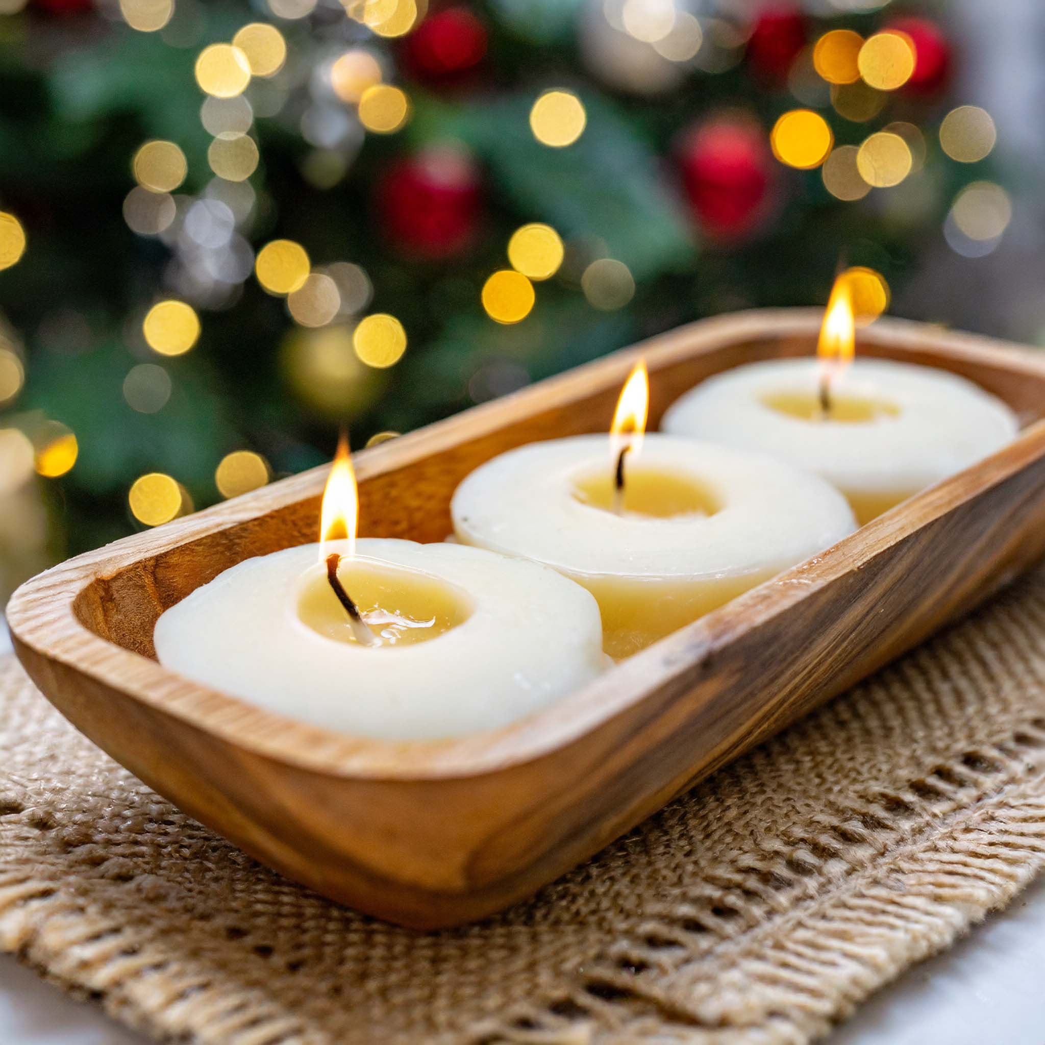 Wooden dough bowl candle with holiday lights in background.