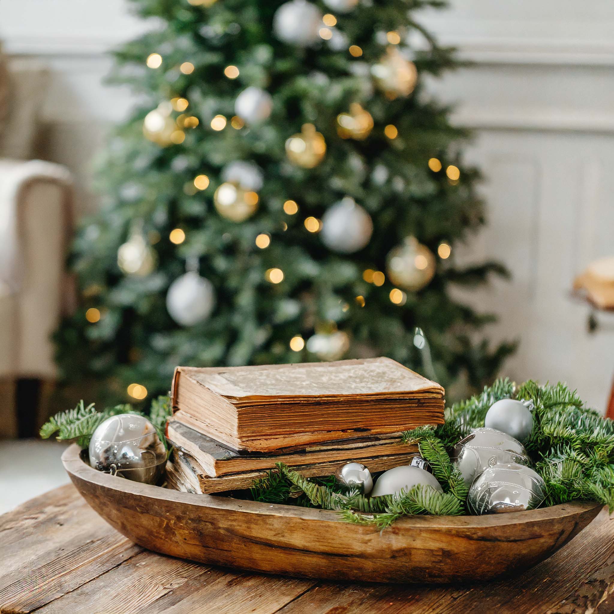 Wooden dough bowl filled with vintage books, greenery, and vintage Christmas ornaments.