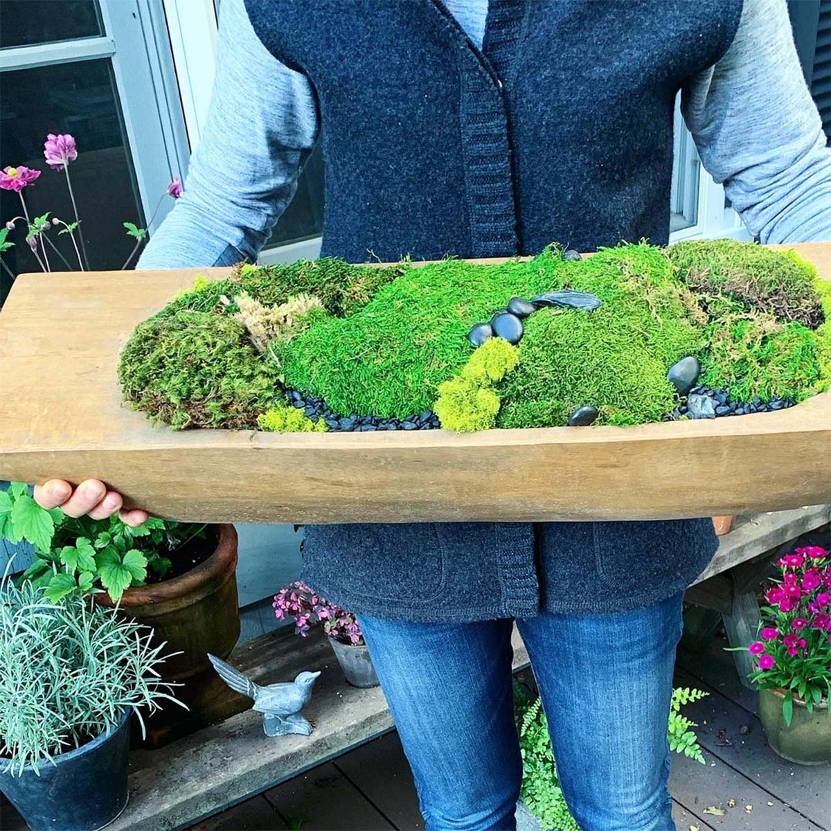 Woman holding wooden dough bowl filled with moss and rocks.