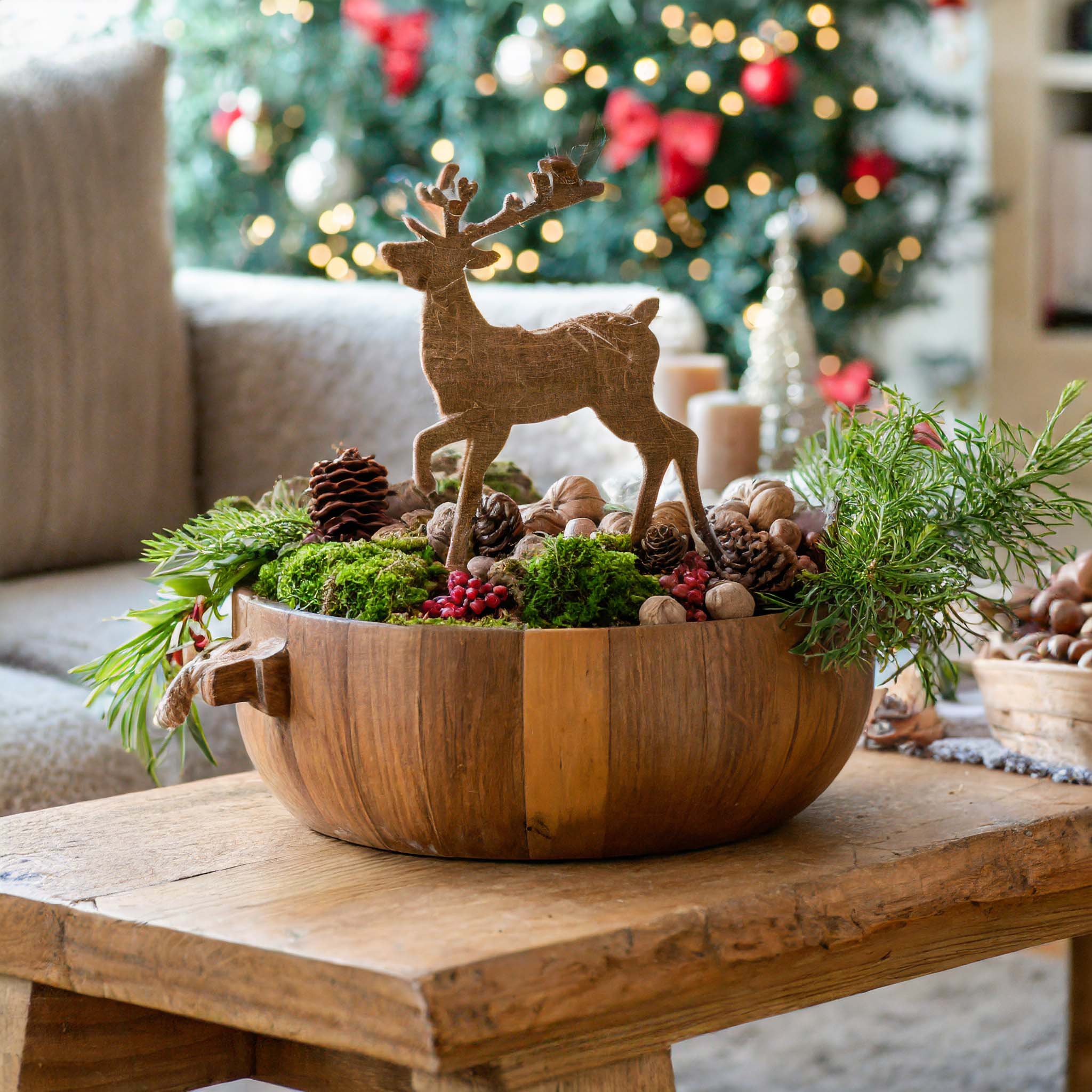 Wooden dough bowl filled with pine cones, a reindeer, moss, walnuts, and berry sprays.