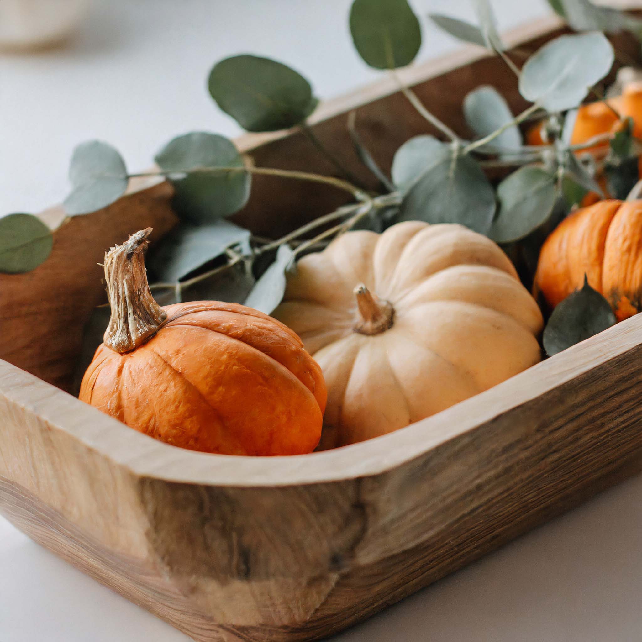 Wooden dough bowl filled with pumpkins and eucalyptus.