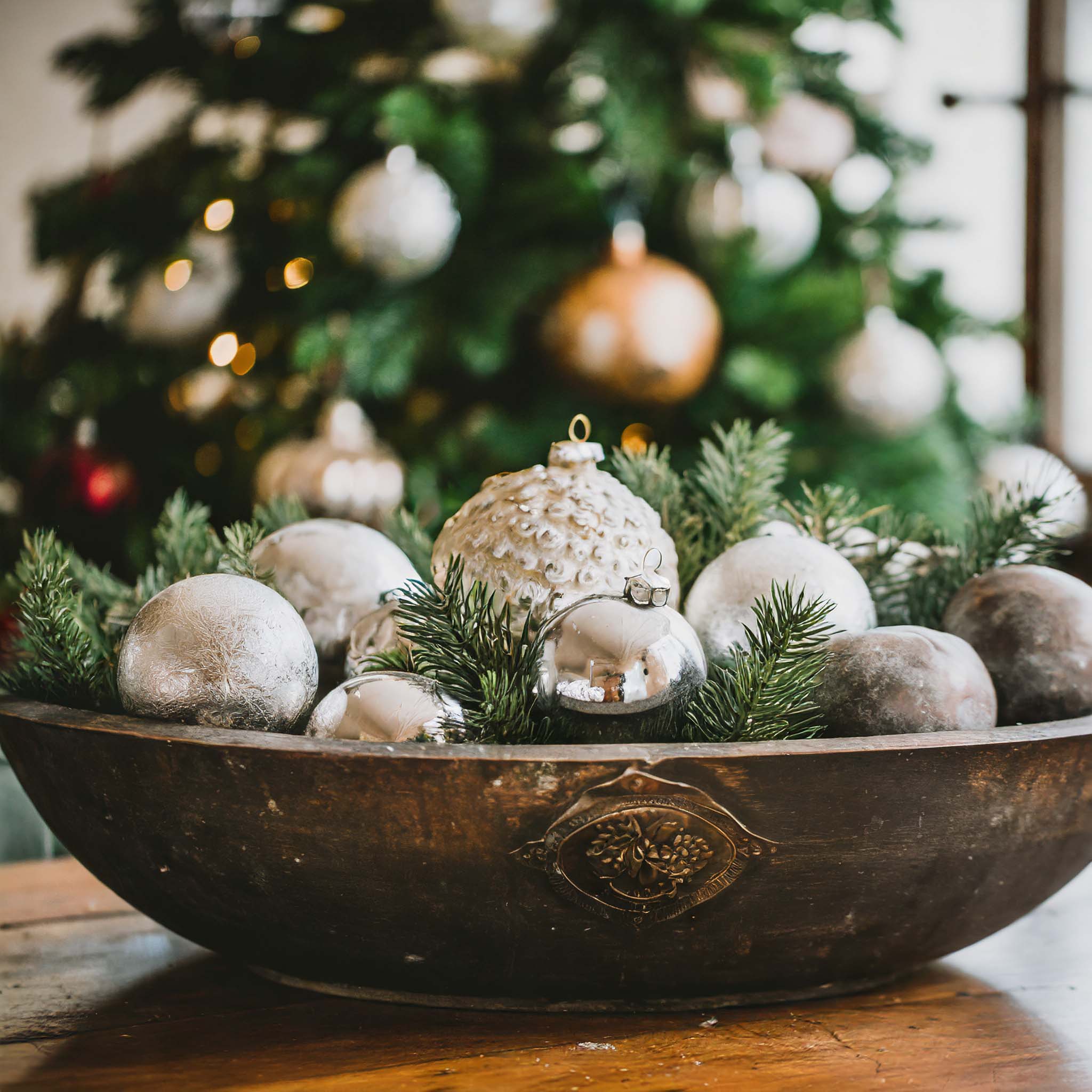 Wooden dough bowl filled with vintage holiday ornaments and greenery.
