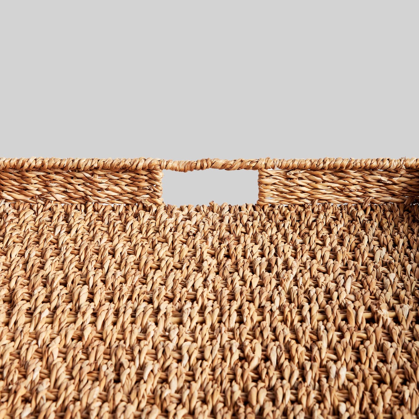 Woven seagrass rectangular tray set, closeup of handle, with gray background.