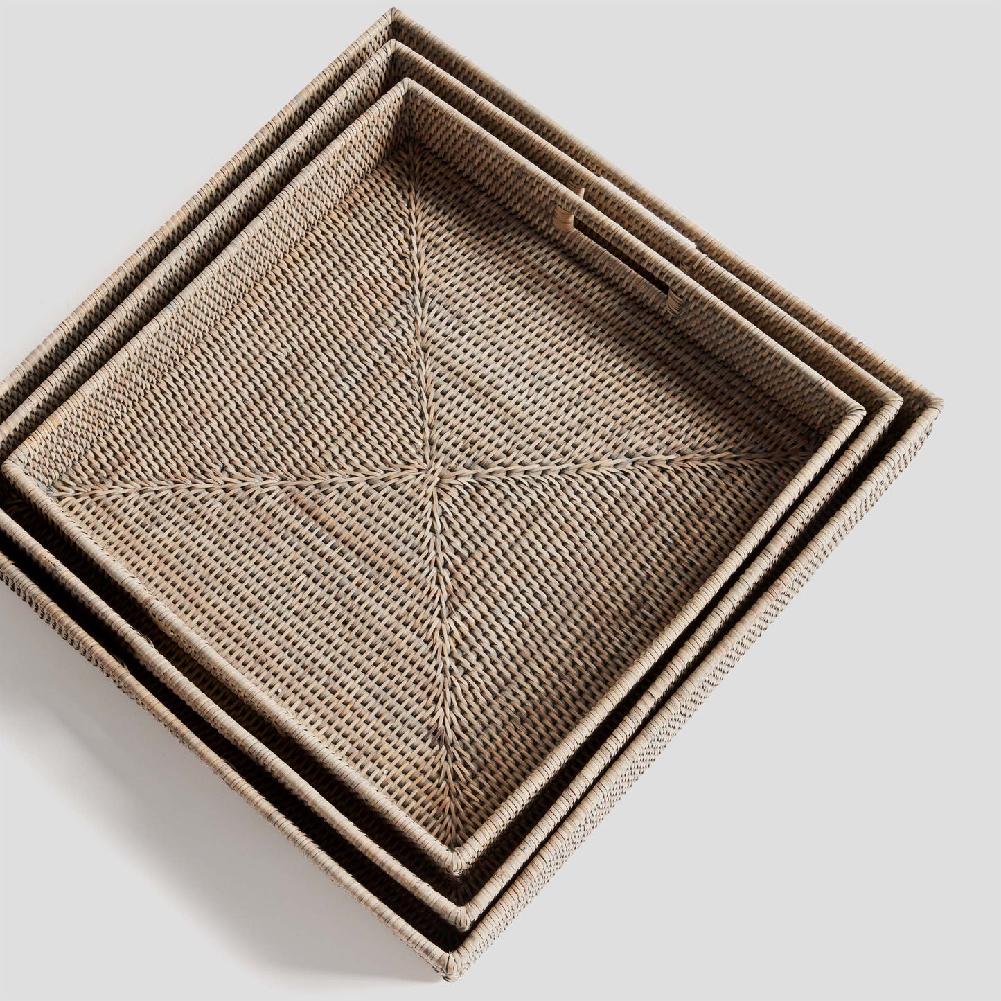 Woven square ottoman tray set in rattan with whitewash finish, nested top view, gray background.