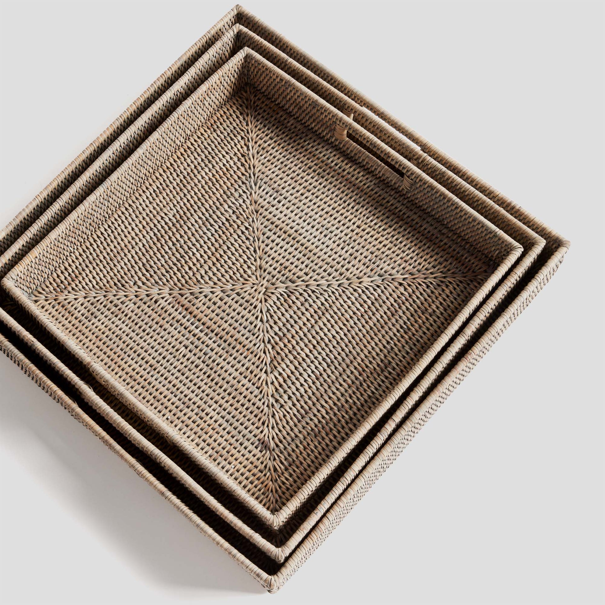 Woven square ottoman tray set in rattan with whitewash finish, nested top view, gray background.
