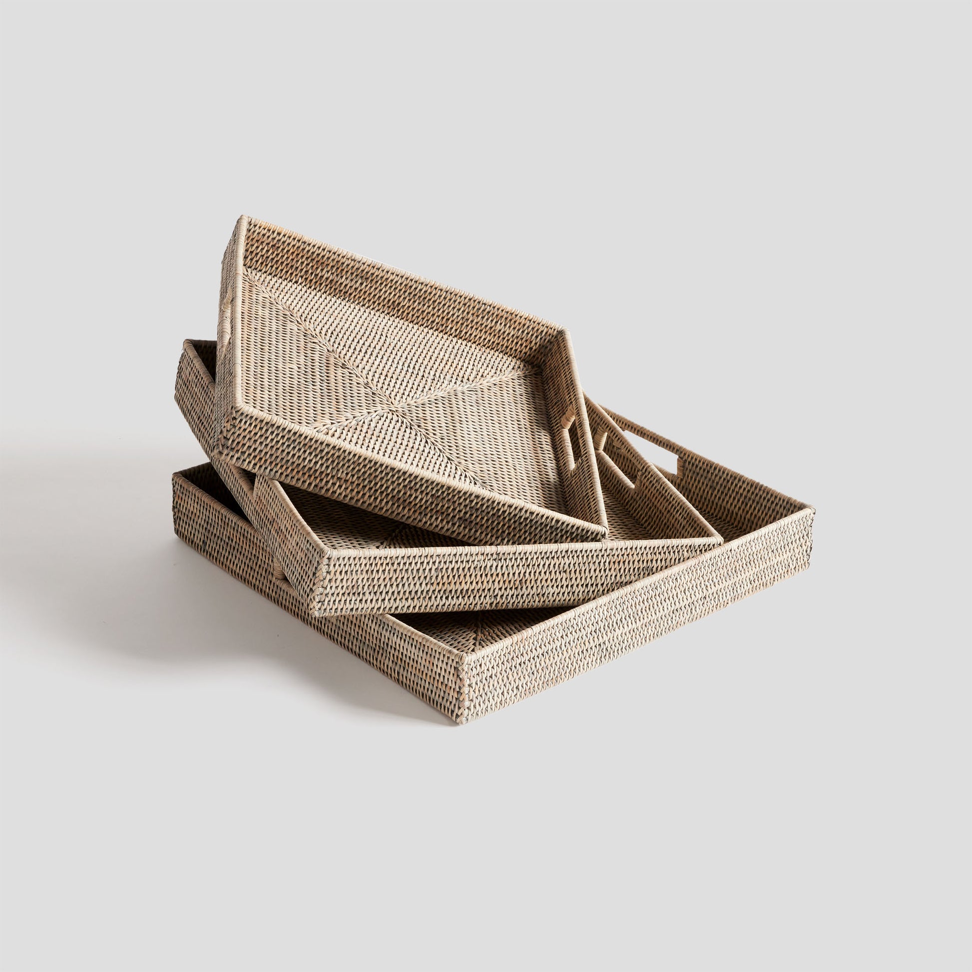 Woven square ottoman tray set in rattan with whitewash finish, stacked, gray background.