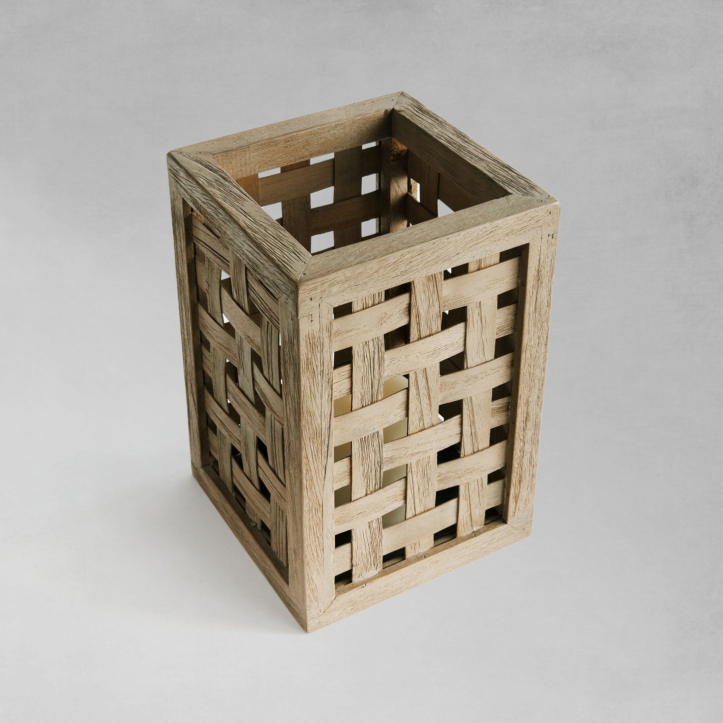 Top view of woven teak hurricane candleholder with gray background.