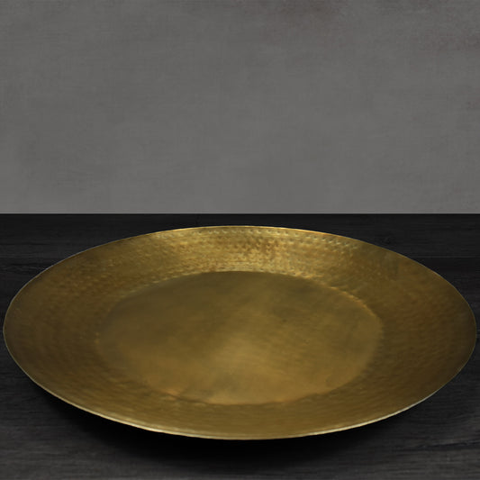 Round antiqued brass metal hammered tray on dark wooden floor.