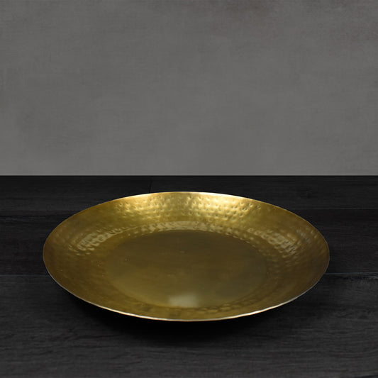 Round antiqued brass metal hammered tray on dark wooden floor.