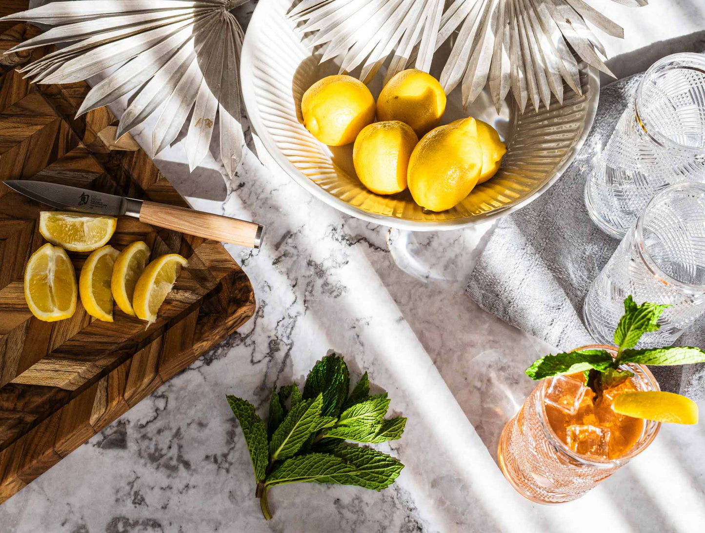 Artesa ceramic bowl/vessel with lemons, tea, and mint with sun-palms on marble table.