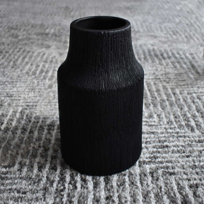Matte black textured ceramic vase on black, white, and gray geometric rug.