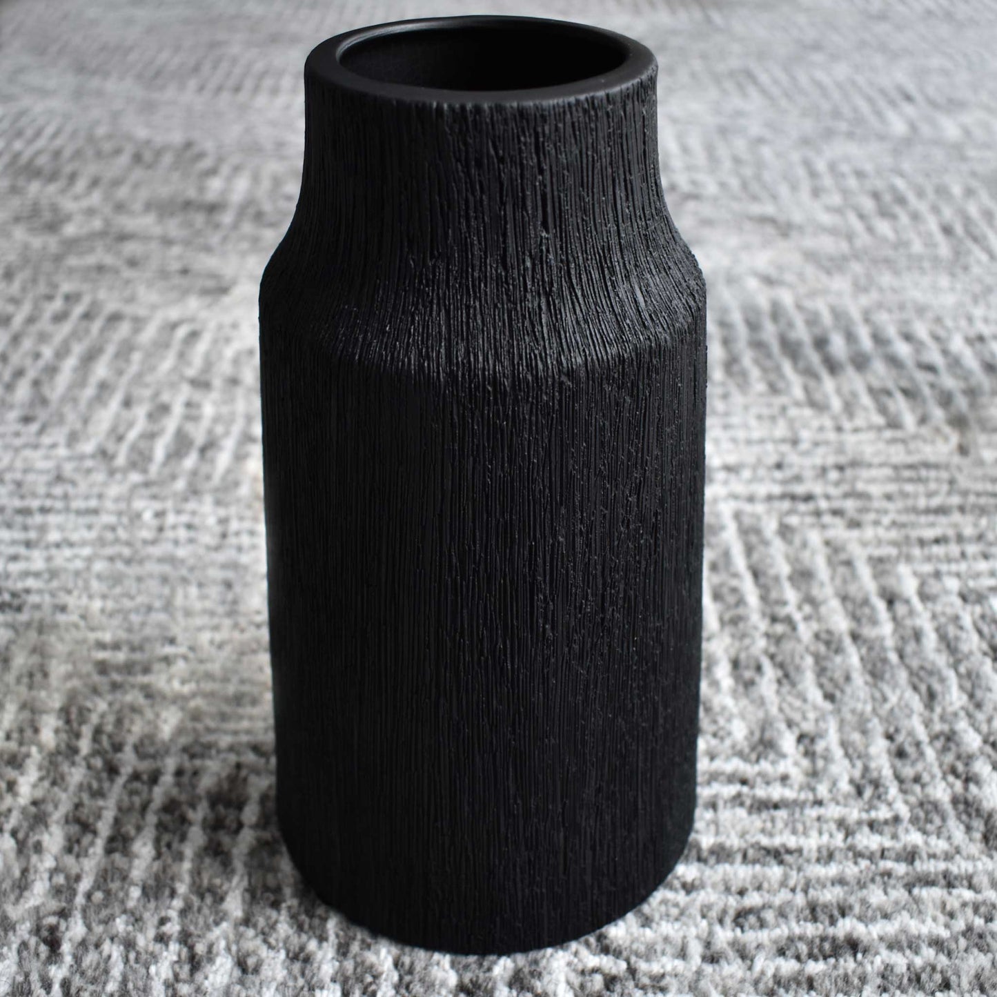 Black ceramic textured vase on black, white, and gray geometric rug.
