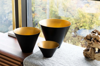 Black and gold metal bowls on walnut console table in front of window.