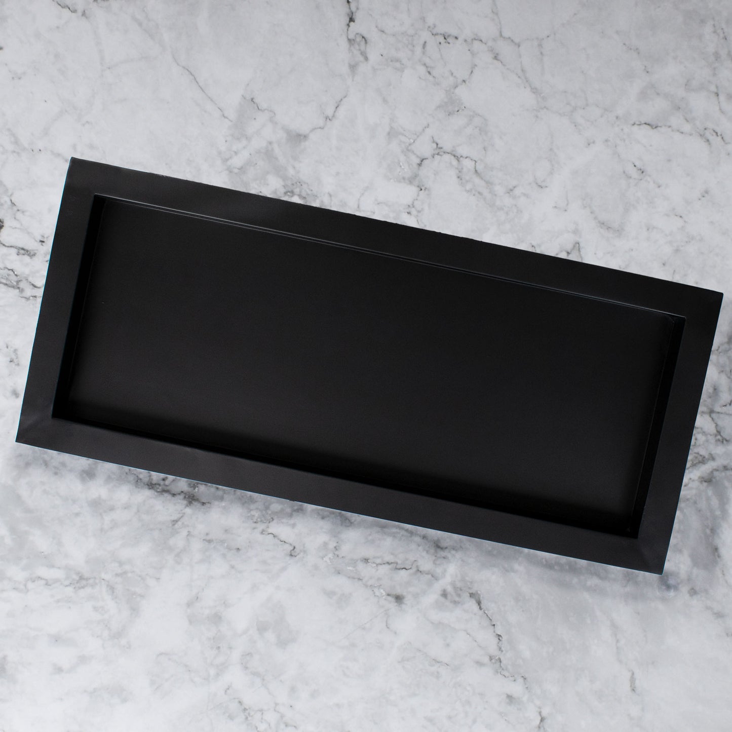 Black matte metal centerpiece tray on marble countertop.