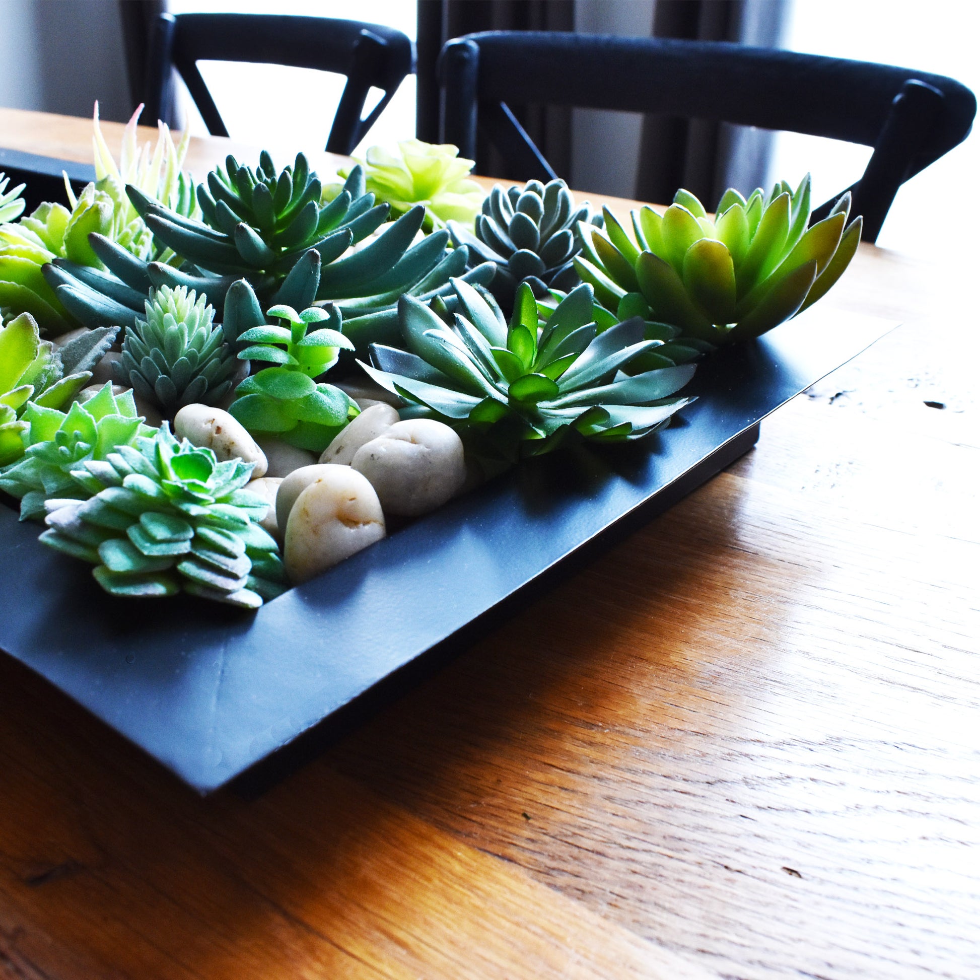 Black matte metal centerpiece tray with succulents on farmhouse table with black oak bistro chairs.