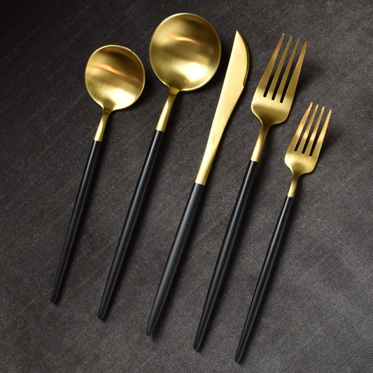 Brushed gold and black handle flatware on dark grey fabric background.