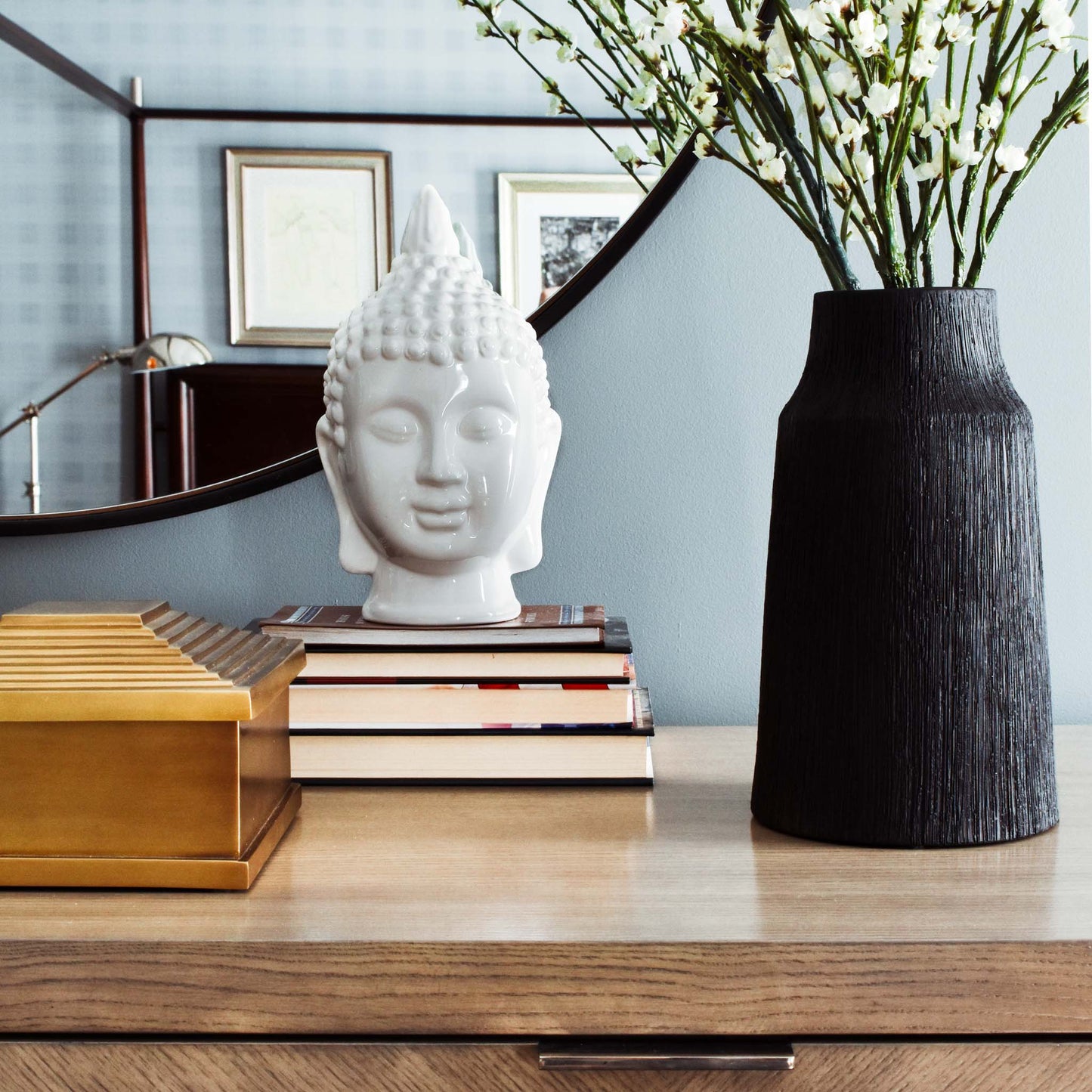 Matte black textured base with cherry blossom branches, brass pyramid box, and Buddha bust on stack of books.